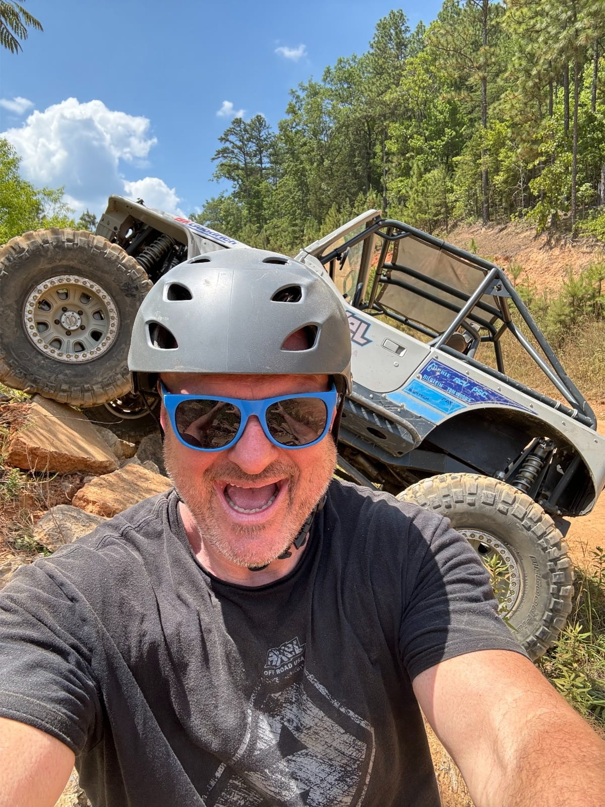 Man with helmet and sunglasses in front of an off-road vehicle on a trail